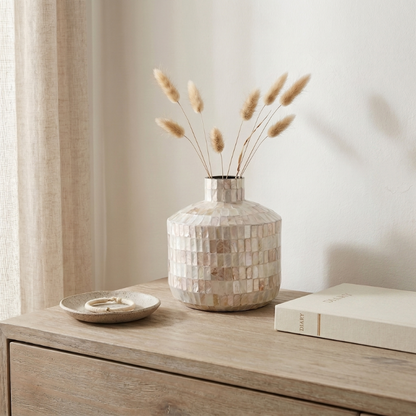 Coastal shell mosaic vase with dried stems on wooden dresser