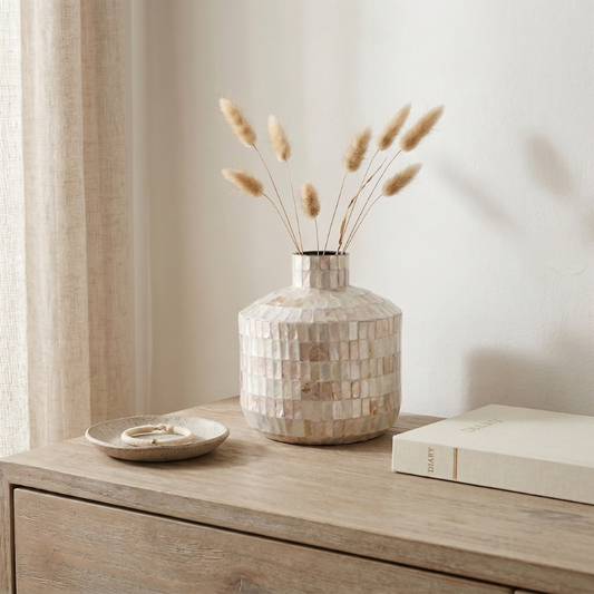 Coastal shell mosaic vase with dried stems on wooden dresser
