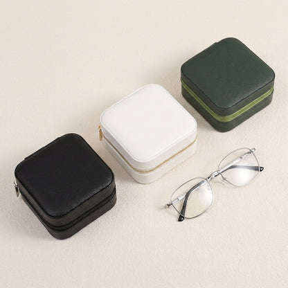 Black, white, and forest green jewelry organizer cases beside a pair of glasses