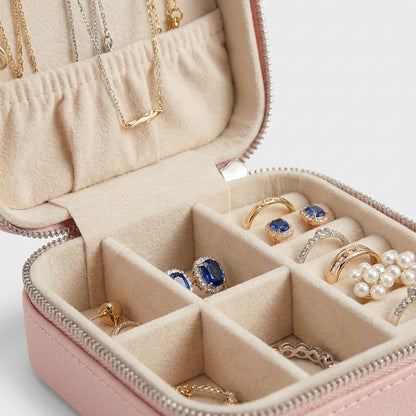 Close-up of an open light pink jewelry case showing necklaces, rings, and an earring in its compartments