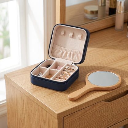 Open navy jewelry case on a wood vanity beside a hand mirror, showing rings in its compartments