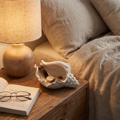 White ceramic conch shell vessel on a bedside nightstand holding a watch and jewelry, Kiyo Home