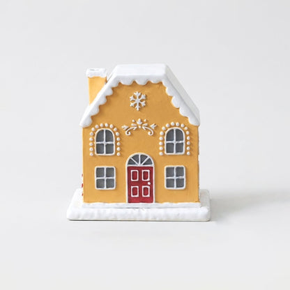 Yellow and white gingerbread-style cottage incense burner with a red door, snow-capped roof, and chimney, on a plain studio background