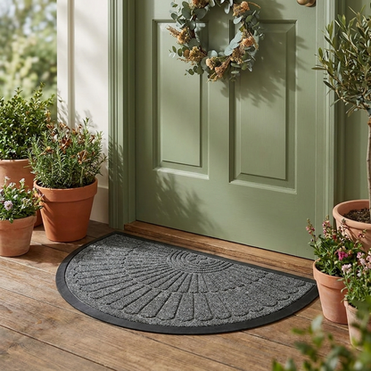 Grey crescent half-moon door mat on a front porch by a green front door with potted plants