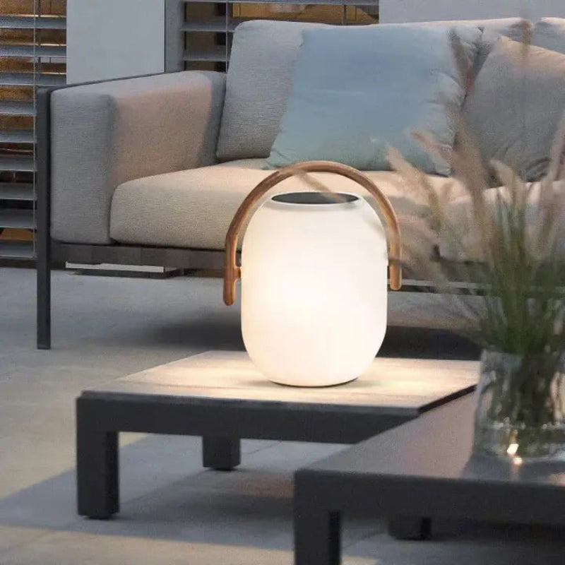 White outdoor lamp with wooden handle on a table in an outdoor setting