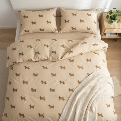 Dachshund-print duvet and pillows on a bed beside a nightstand with a potted plant