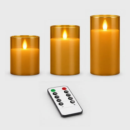 Three amber tinted flameless candles of different heights with a remote control on a plain light background