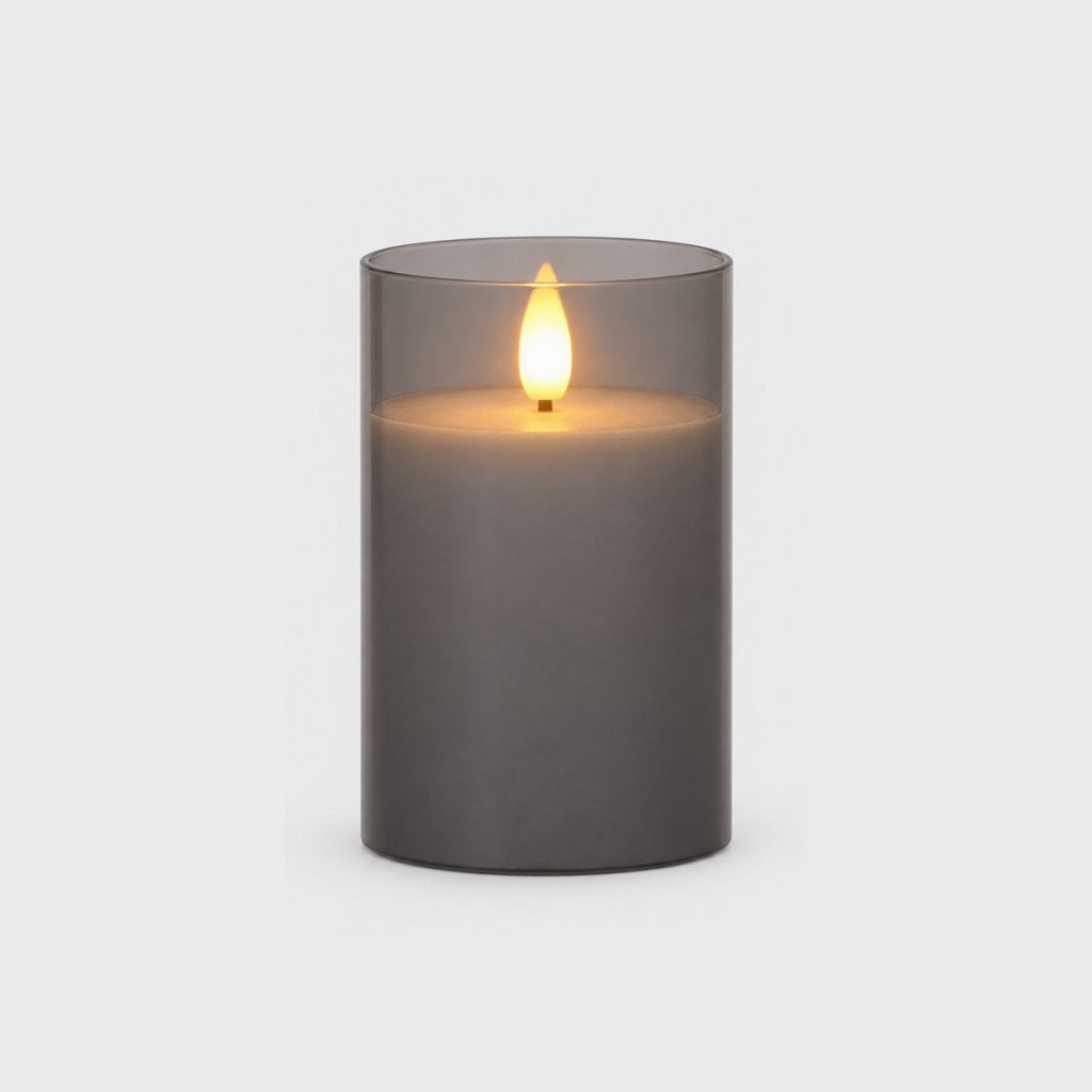 Medium grey tinted flameless candle with a glowing flame on a plain light background