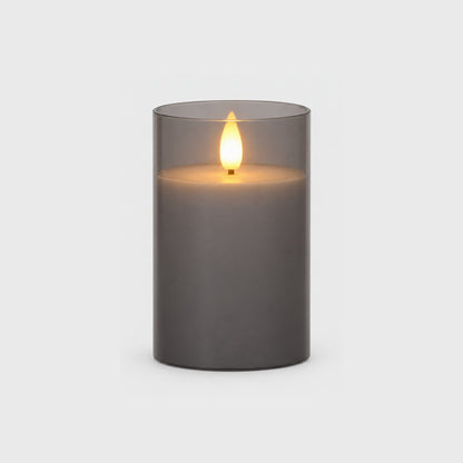 Medium grey tinted flameless candle with a glowing flame on a plain light background