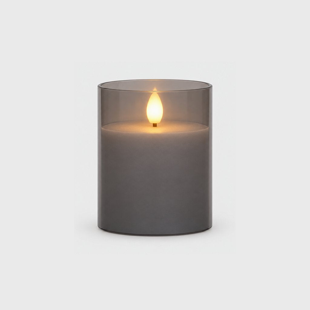 Small grey tinted flameless candle with a glowing flame on a plain light background