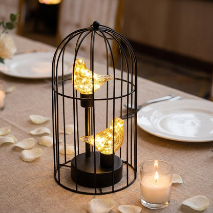 Two Birds illuminated birdcage on a set dinner table with candles and scattered rose petals