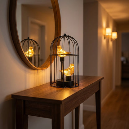 Two Birds illuminated birdcage on a console table beneath a round mirror in a hallway