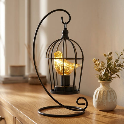 Single Bird illuminated birdcage on a sideboard beside a vase of dried plant sprigs