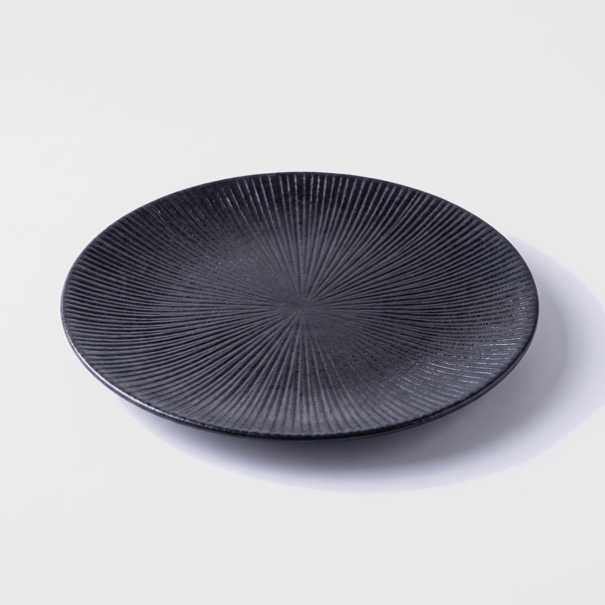 Black disc ceramic dinner plate with radial ridged design on an off-white background