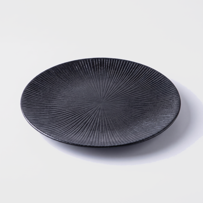 Black disc ceramic dinner plate with radial ridged design on an off-white background