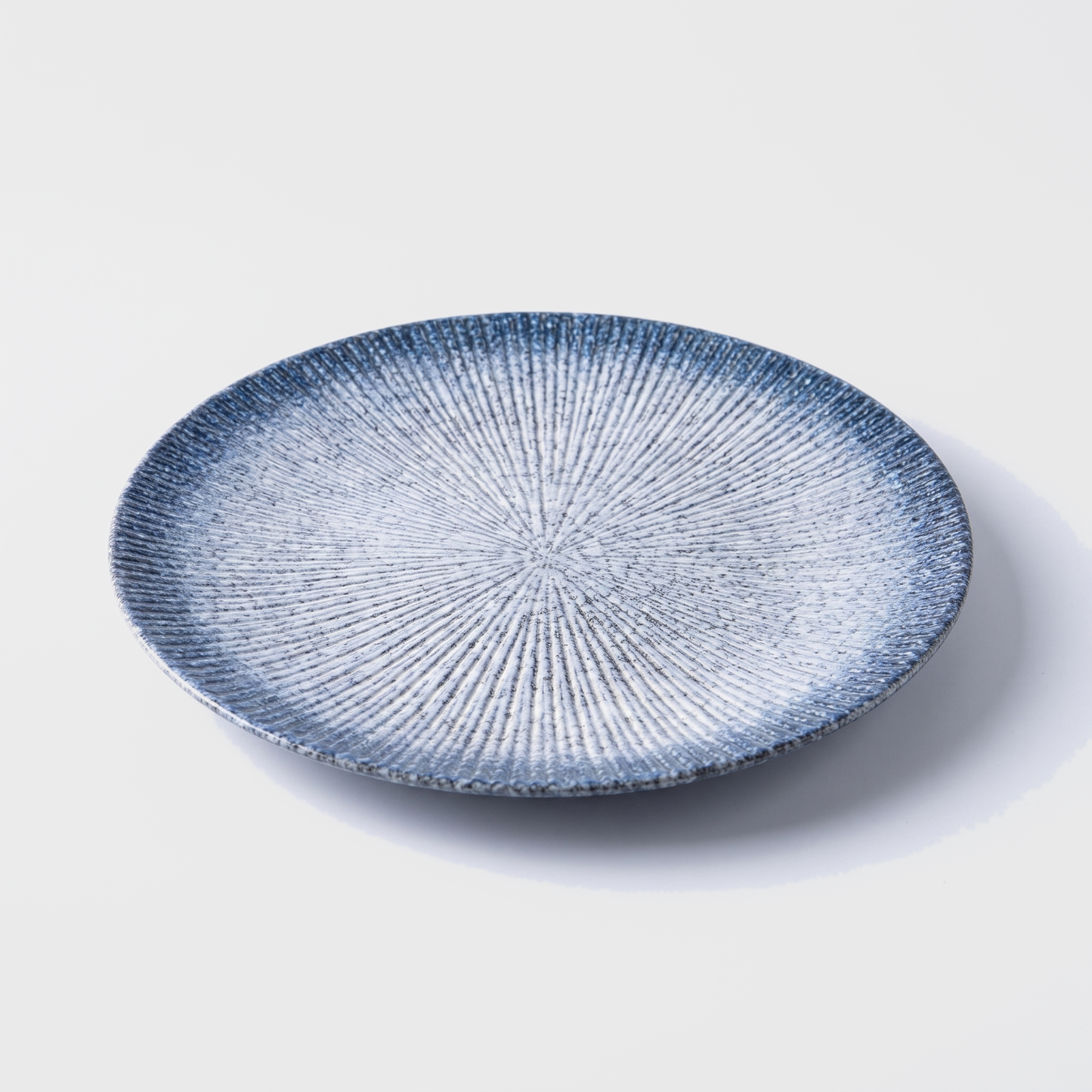 Blue disc ceramic dinner plate with radial ridged design on an off-white background