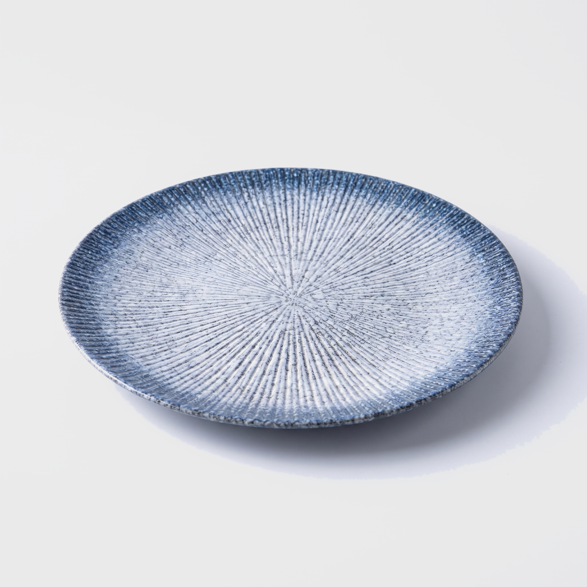 Blue disc ceramic dinner plate with radial ridged design on an off-white background