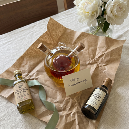 Dual oil and vinegar bottles on kitchen table with bread and herbs