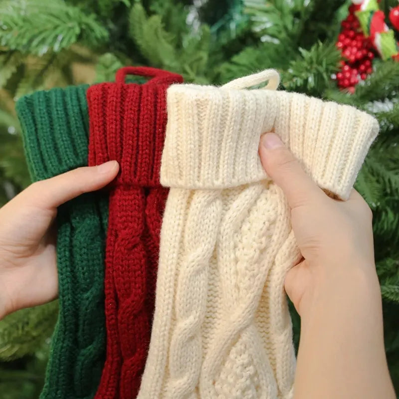Hands holding green, red, and white knitted Christmas stockings.
