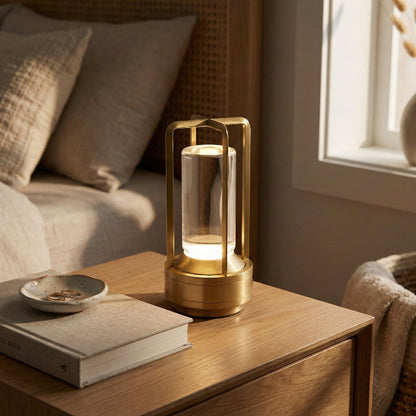 Gold lantern on a wooden table with a book and small dish in a cozy room.