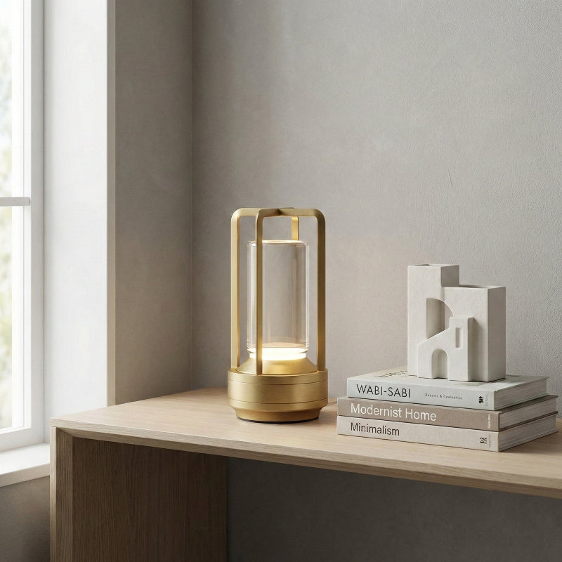 Gold table lamp on a wooden surface with books and decorative items in a minimalistic setting.