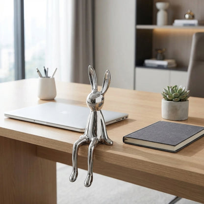 Metallic rabbit-shaped object on a desk with a laptop and plant in the background