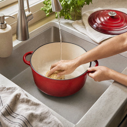 Red enameled Dutch oven being hand-washed in a kitchen sink