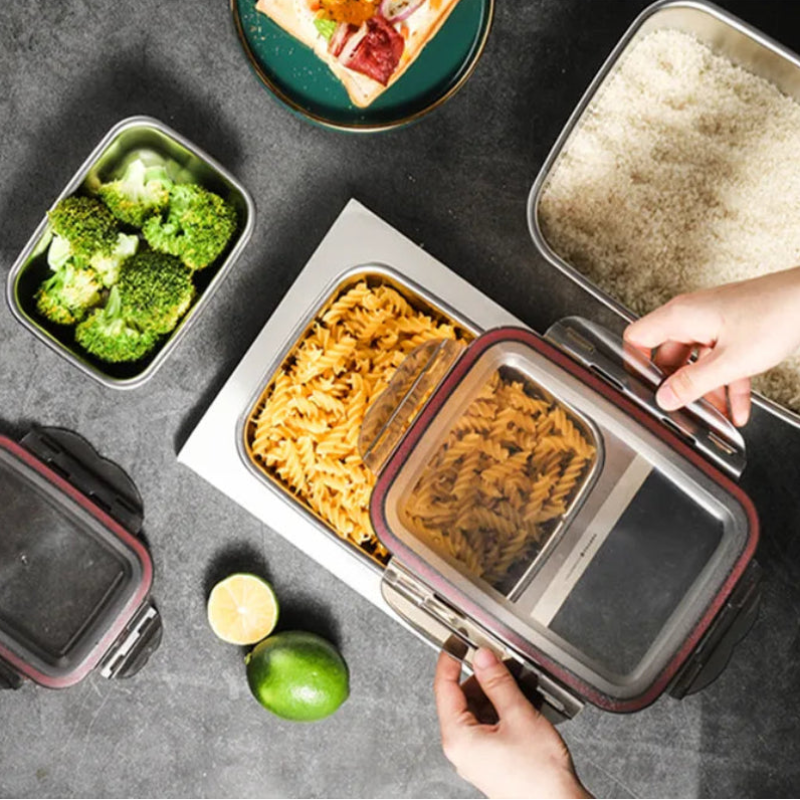 Hands open a large stainless steel food container with nested compartments of pasta and rice.