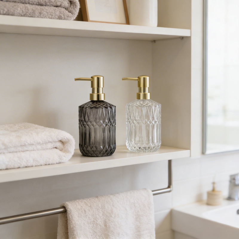 Facet glass soap dispensers on bathroom shelf with folded towels