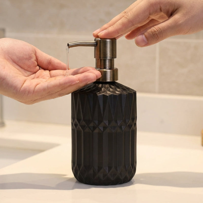 Black facet glass soap dispenser being pressed by hand
