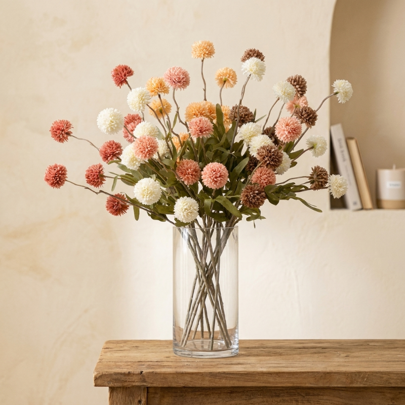 Peach faux dandelion stems in clear glass vase on wooden table
