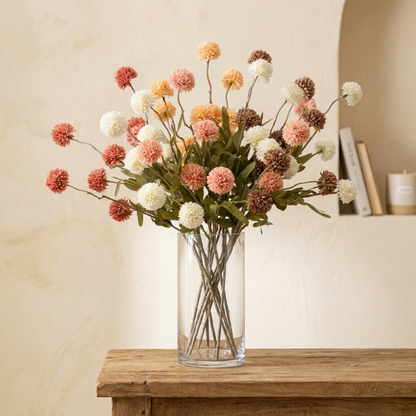 Peach faux dandelion stems in clear glass vase on wooden table
