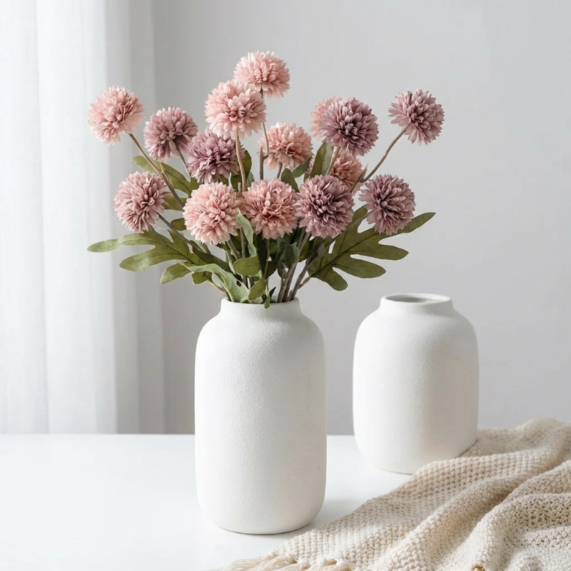Pink faux dandelion stems in white vases on neutral surface