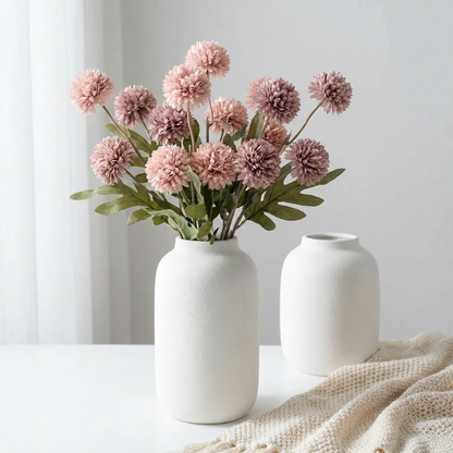Pink faux dandelion stems in white vases on neutral surface
