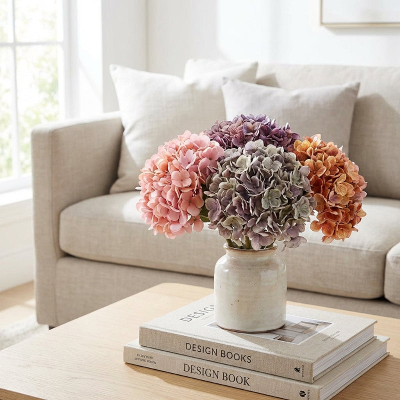Vase of multicolored hydrangeas on design books with a beige sofa in the background