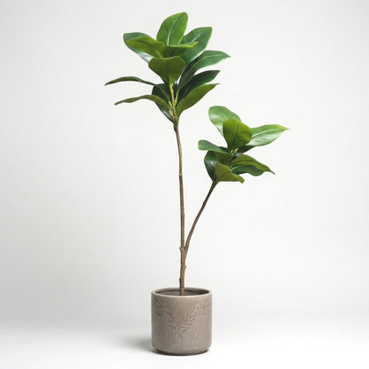 Two faux magnolia tree stems in a taupe ceramic pot with an embossed leaf pattern, on a plain studio background