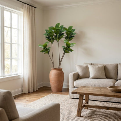 Faux magnolia tree in a terracotta urn in a living room corner beside a linen sofa and wood coffee table