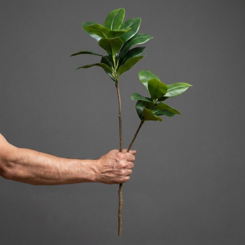 Hand holding two faux magnolia tree stems by their bases on a plain studio background