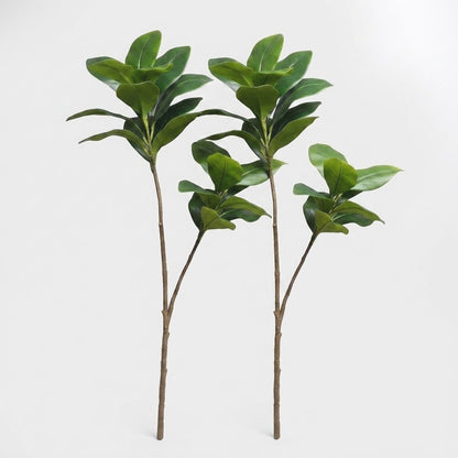Two faux magnolia tree stems standing side by side on a plain studio background