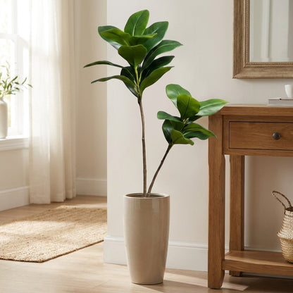 Two faux magnolia tree stems in a glossy cream tapered planter in an entryway beside a console table and mirror