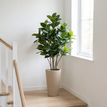 Bushy faux magnolia tree in a tall beige tapered planter on a staircase landing beside a white railing