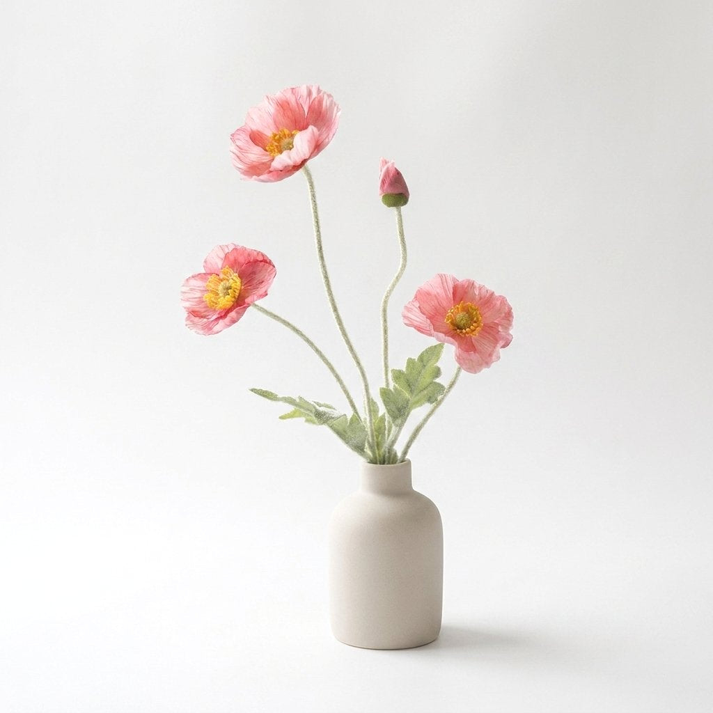 Four faux poppy stems with three salmon-coral pink blooms with deeper pink edges and a bud in a cream ceramic bottle vase on a plain light backdrop