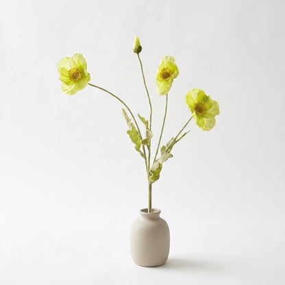 Four faux poppy stems with three pale lime yellow-green blooms and a lime bud in a matte taupe ceramic jar on a plain light backdrop