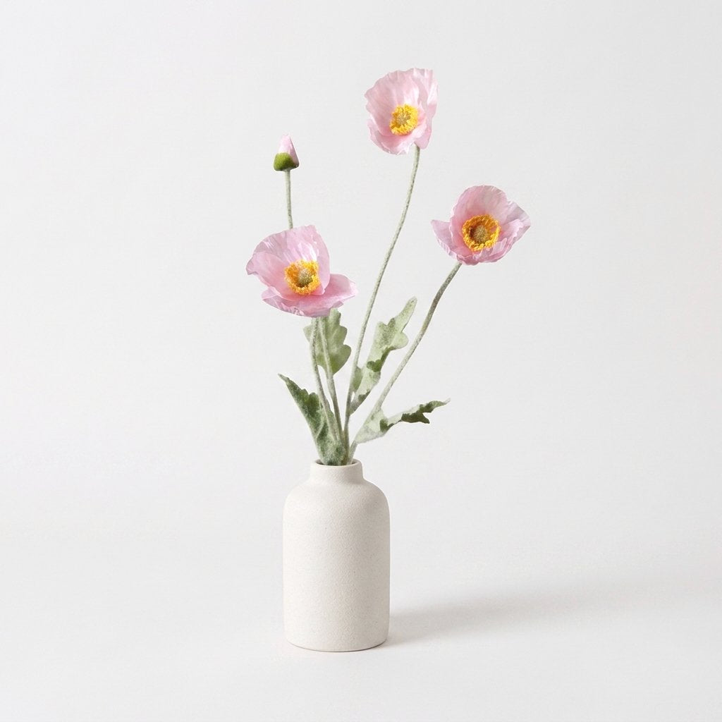 Four faux poppy stems with three pale pink blooms with yellow-gold centers and a pale pink bud in a speckled cream stoneware bottle vase on a plain light backdrop