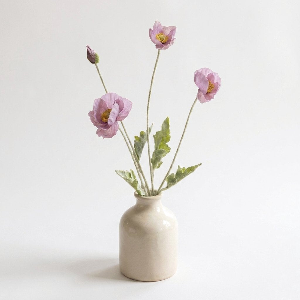 Four faux poppy stems with three dusty mauve blooms and a mauve-purple bud in a glossy cream ceramic jar vase on a plain light backdrop