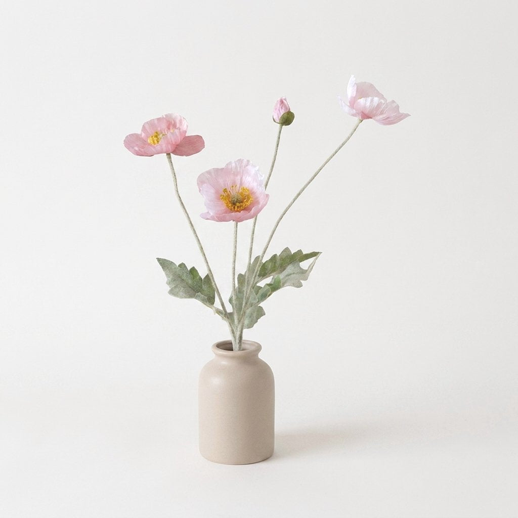 Four faux poppy stems with three soft pastel pink blooms and a bud in a beige ceramic jar vase on a plain off-white backdrop