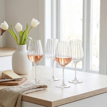Wine glasses with rose wine on a table with a vase of tulips and cheese.