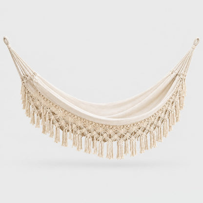 Cream fringe macrame hammock with a diamond netting border and knotted fringe, with a looped hanging cord at each end, on a plain light gray background