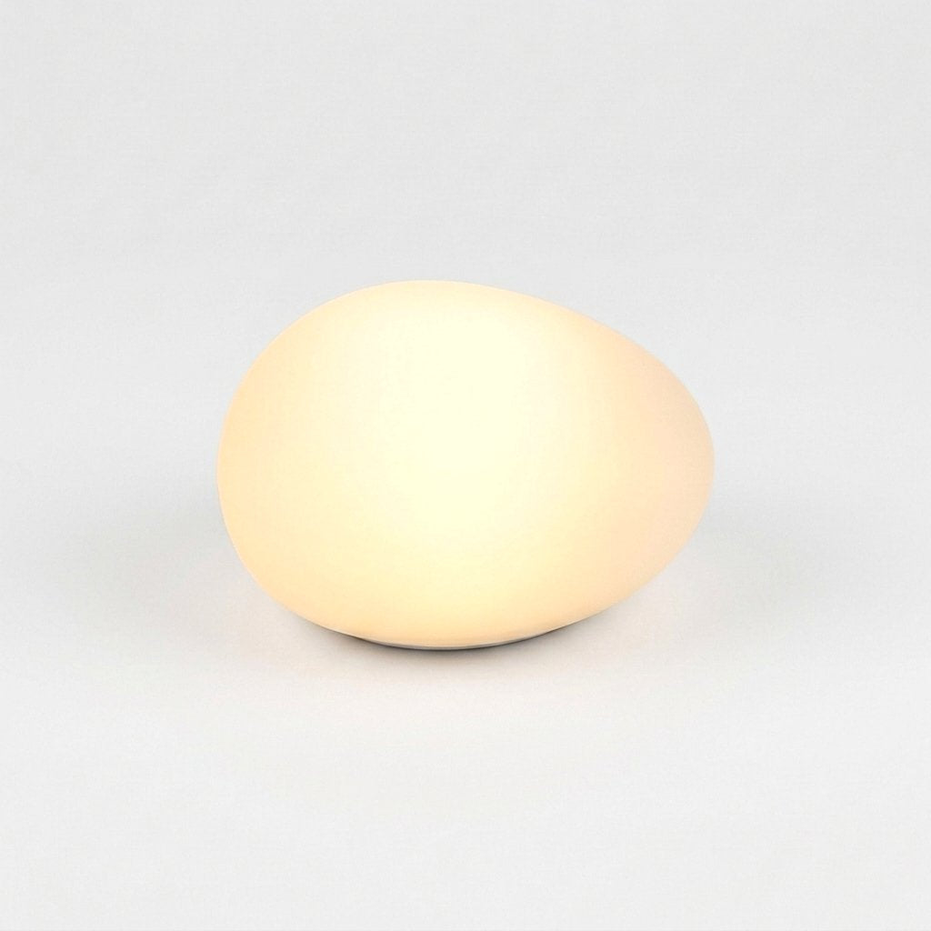 One frosted solar glass pebble light glowing warm yellow on a light background
