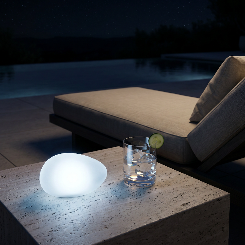 Frosted solar glass pebble light glowing on outdoor side table by lounge chair